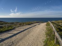 the path has a wooden fence with railings on it leading to a beach that overlooks the water