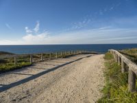 the path has a wooden fence with railings on it leading to a beach that overlooks the water