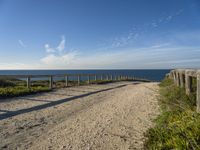 the path has a wooden fence with railings on it leading to a beach that overlooks the water