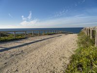 the path has a wooden fence with railings on it leading to a beach that overlooks the water