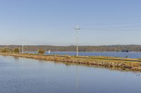 a body of water with power poles on top and utility lines above the waters in the background