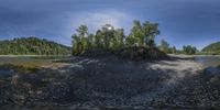 a big pile of dirt sitting next to a river and forest area filled with trees