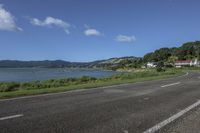 a street near a body of water near some houses on a hill side line with hills and a field in front