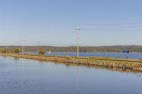 a railroad line on a river with power lines near by and a road near water