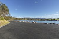 a long asphalt road with a body of water in the background and a sky with clouds