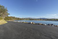 a long asphalt road with a body of water in the background and a sky with clouds