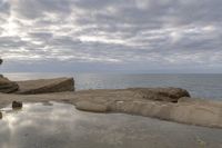 the person is sitting on the rock near the water and clouds over the ocean and it has a bright light