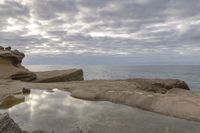 the person is sitting on the rock near the water and clouds over the ocean and it has a bright light