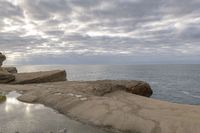 the person is sitting on the rock near the water and clouds over the ocean and it has a bright light