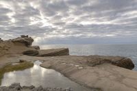 the person is sitting on the rock near the water and clouds over the ocean and it has a bright light