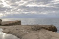 the person is sitting on the rock near the water and clouds over the ocean and it has a bright light