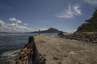 rocks on the ocean shore near a rock wall and an island with trees in the distance