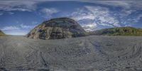 a 360 camera photo of the ocean waves and sand in a body of water, in front of a rock