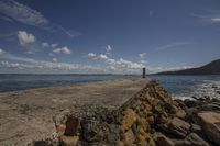 the water and rocks are beside the beach with clouds in the sky and a large rock wall