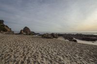 a rocky beach with sand and water at dusk in the distance, with rocks on the shore