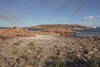 a body of water next to a rocky beach with bushes and rocks on both sides of it