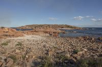 a body of water next to a rocky beach with bushes and rocks on both sides of it