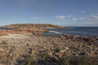 a body of water next to a rocky beach with bushes and rocks on both sides of it