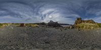 a beach with a rocky shore and large mountain in the background, in a 360 - point lens