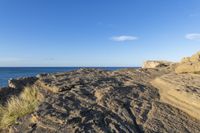 a rocky cliff near the ocean with some waves on it, and blue skies above