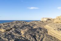 a beach and rocky outcropping next to the ocean and sky with an airplane flying