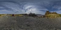 a beach with a rocky shore and large mountain in the background, in a 360 - point lens