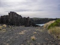 a rocky shore with grass and dirt, on a sunny day with a cloudy sky