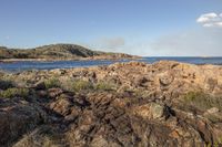 a view of the ocean from a rocky shoreline next to a beach with some rocks