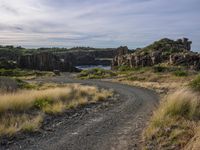 a dirt road with rocks at the end of it and water in the distance behind