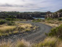 a dirt road with rocks at the end of it and water in the distance behind