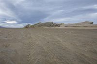 a sand dune is near some rocks and in front of some clouds with a dark blue sky