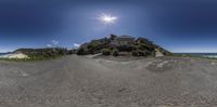 a fish eye view of a house and sand dunes with beach in the background, and bright sunshine streaming through the blue sky