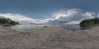 a panoramic image shows the sand dunes next to a body of water and a lighthouse in the distance