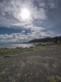 the bright sun shines through the clouds as a bike rests on a gravel field by the ocean