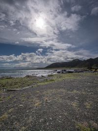 the bright sun shines through the clouds as a bike rests on a gravel field by the ocean