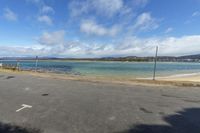 a paved parking lot with water and mountains in the background at low tide, surrounded by parked cars