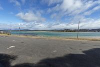 a paved parking lot with water and mountains in the background at low tide, surrounded by parked cars