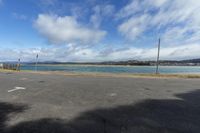 a paved parking lot with water and mountains in the background at low tide, surrounded by parked cars