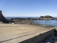 a sandy beach next to the ocean with a boat on it's shore and rock walls