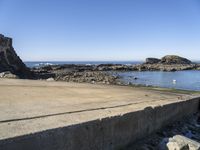 a sandy beach next to the ocean with a boat on it's shore and rock walls