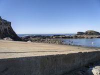 a sandy beach next to the ocean with a boat on it's shore and rock walls