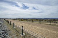 a dirt road and fenced in area with mountains behind it, and blue sky with white clouds