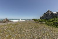 a sandy beach and cliffs near the ocean and trees with blue sky behind them, with rocky area