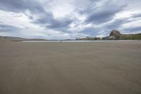 a cloudy sky over a beach covered in sand and hills under a cloudy blue sky