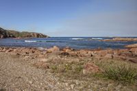 rocks and gravel on a rocky beach with blue skies above them and a blue sky in the distance