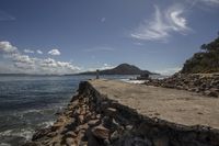 an empty sandy beach and a lone rock wall by the ocean and a mountain in the distance