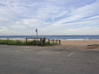 a sandy beach with two parking spots and a bench overlooking the ocean on the other side