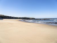 the beach has sand, water, and rocks at high tide watershore with ocean spray, houses, sand, and blue sky