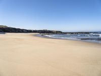 the beach has sand, water, and rocks at high tide watershore with ocean spray, houses, sand, and blue sky