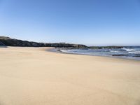 the beach has sand, water, and rocks at high tide watershore with ocean spray, houses, sand, and blue sky